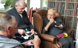 three senior friends eating cake at a care home